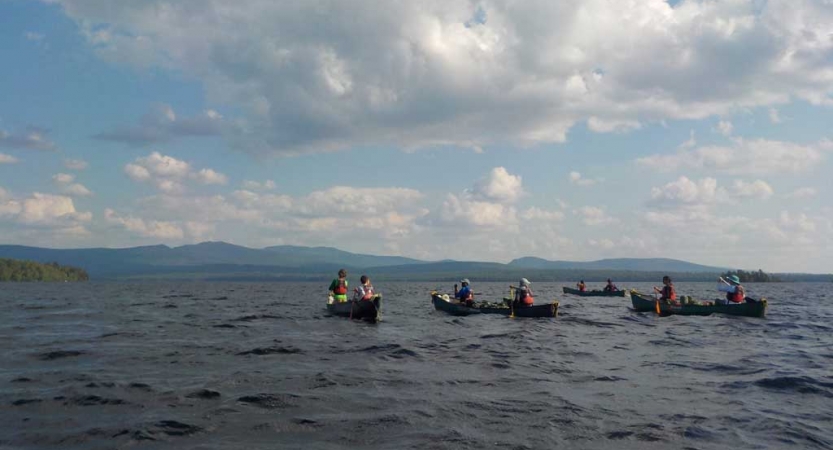 Four canoes are paddled on choppy water. There are mountains in the distance. 